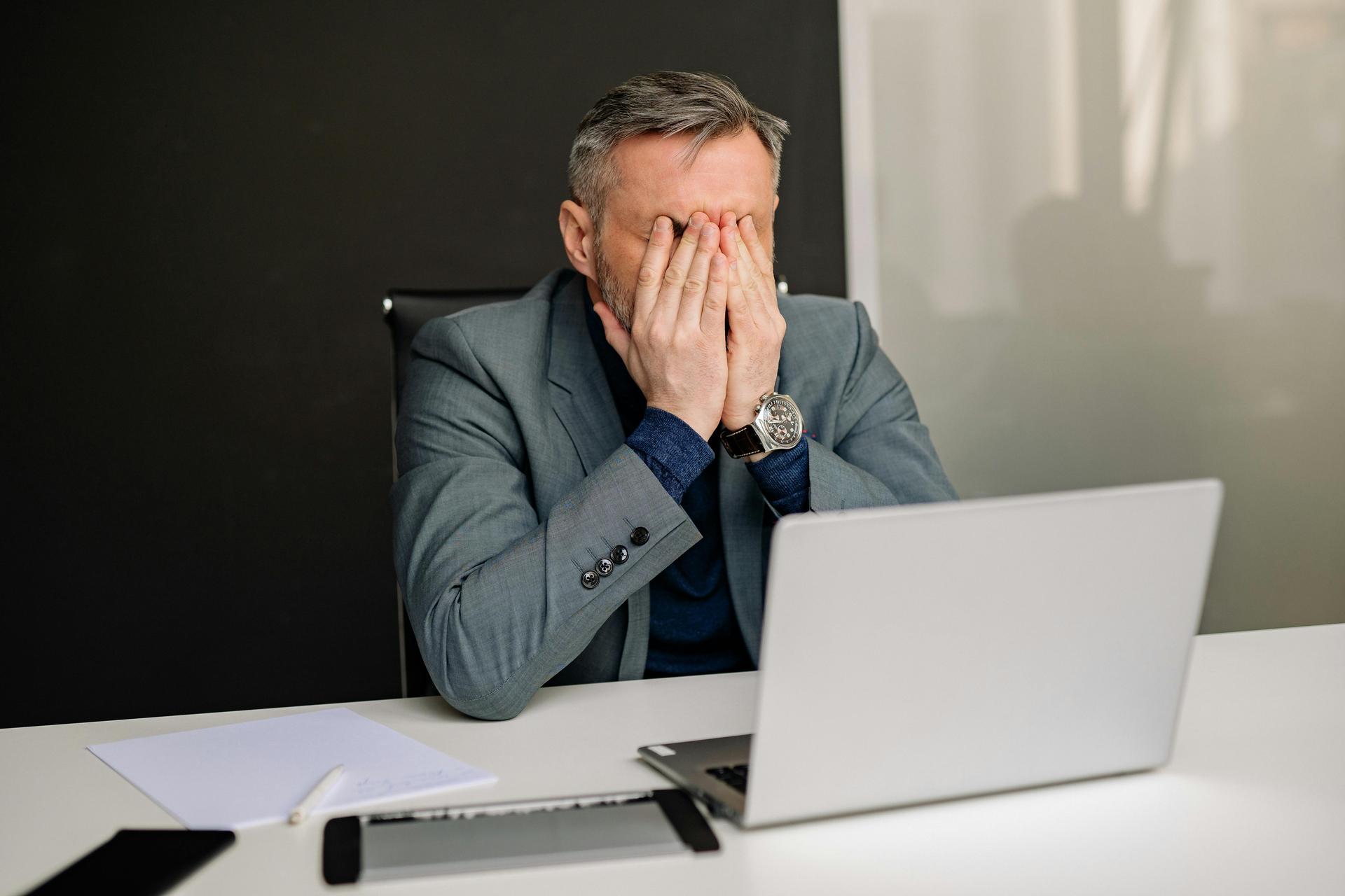 man with a headache in front of his laptop