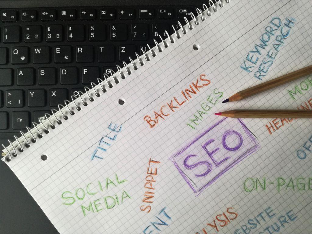 A notebook beside a keyboard with SEO terms like keywords, backlinks, snippets, and on-page written across the page.