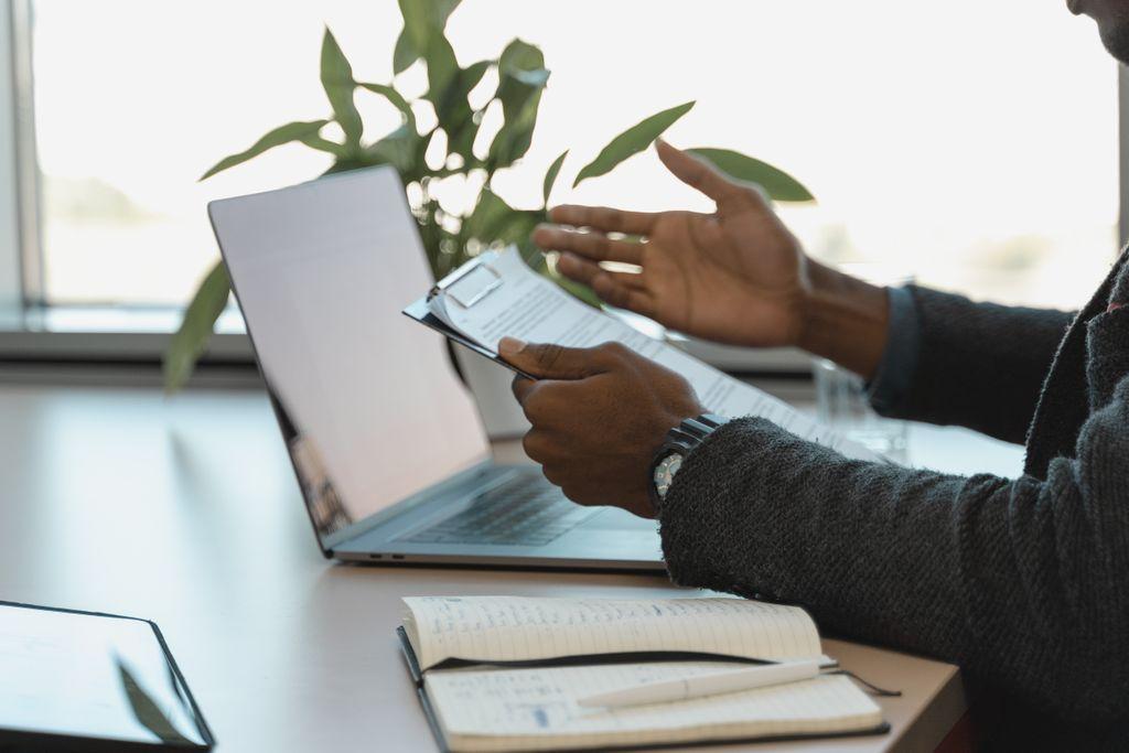 Professional reviewing a report beside a laptop and notebook